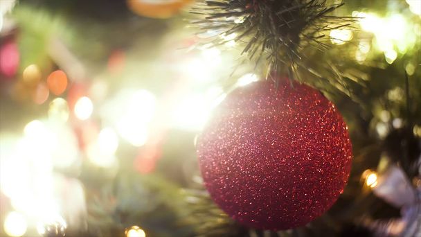 Διακοσμημένο χριστουγεννιάτικο δέντρο σε θολή, αφρώδη και νεράιδα φόντο, Καλά Χριστούγεννα και ευτυχισμένη έννοια του νέου έτους. Σκελετός. Κοντινό πλάνο για κόκκινο λαμπερό μπάλα και φωτίζεται γιρλάντα με φακούς. - Φωτογραφία, εικόνα