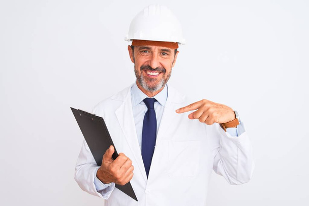 Senior engineer man wearing security helmet holding clipboard over isolated white background with surprise face pointing finger to himself - Valokuva, kuva