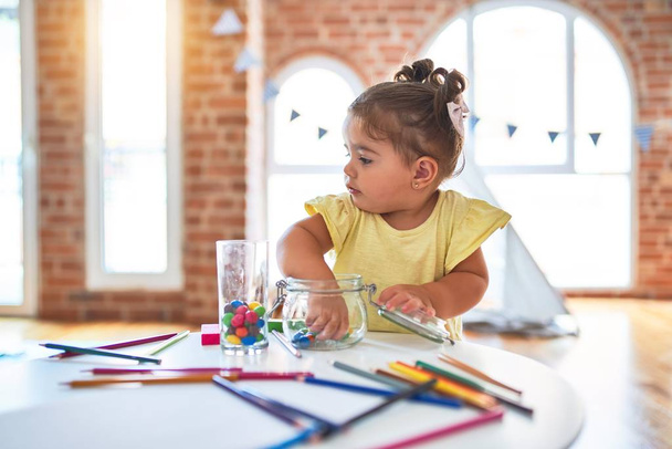 Όμορφο μικρό παιδί στέκεται παίζει με σοκολάτα χρωματιστές μπάλες στο τραπέζι στο νηπιαγωγείο - Φωτογραφία, εικόνα