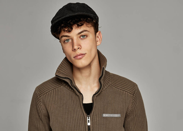 Portrait of handsome teen in knitted sweater and black cap posing in studio - Foto, afbeelding