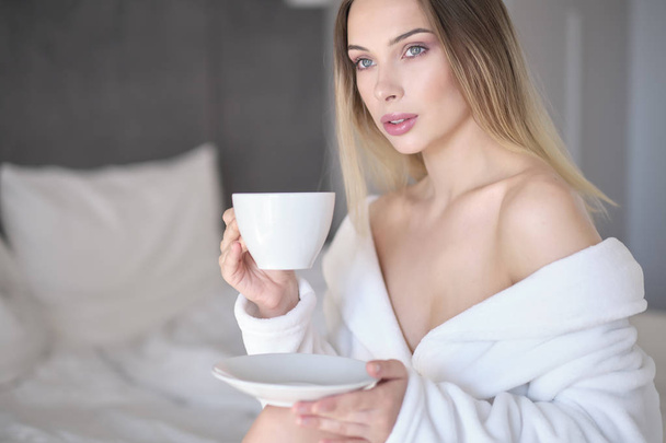 woman in a bathrobe drinks morning coffee in bed - Zdjęcie, obraz