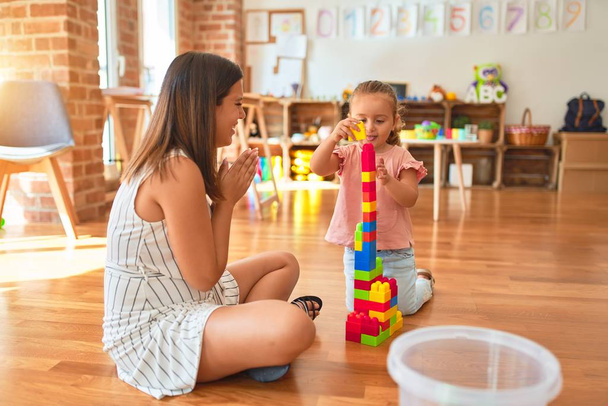 Beautiful teacher and blond toddler girl building tower using plastic blocks at kindergarten - Foto, immagini