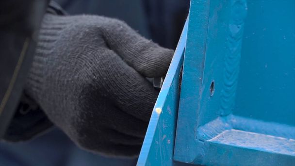 Zárja be a férfi kezét védőkesztyűben lazítja a reteszt egy csavarkulccsal a fém kék szerkezeten. Csípés. A fémszerkezet szétszerelése. - Fotó, kép