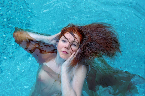 Portrait de belle jeune femme aux cheveux roux flottant joyeusement dans l'eau turquoise dans la piscine
 - Photo, image