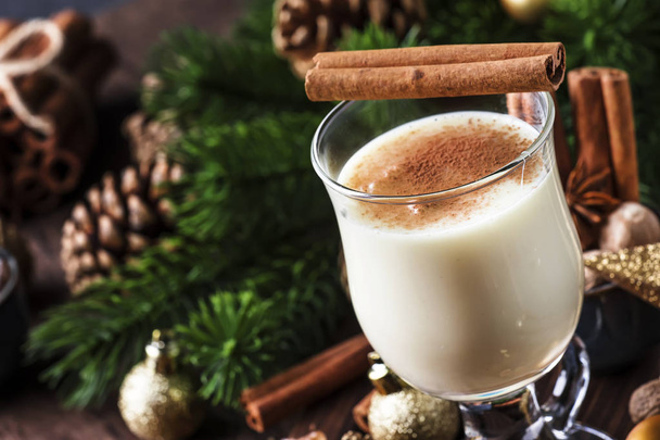 New Year or Christmas Eggnog cocktail - hot winter or autumn drink with milk, eggs and dark rum, sprinkled with cinnamon and nutmeg in a glass on wooden background, festive decoration - Φωτογραφία, εικόνα