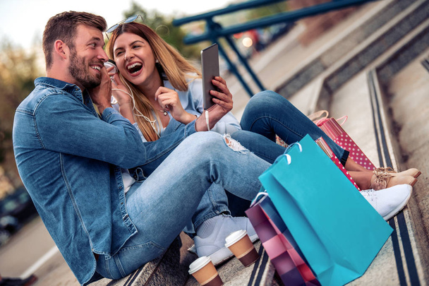 Πορτρέτο του χαμογελαστή ζευγάρι σε εξωτερικούς χώρους, ακούν μουσική μετά τα ψώνια. - Φωτογραφία, εικόνα