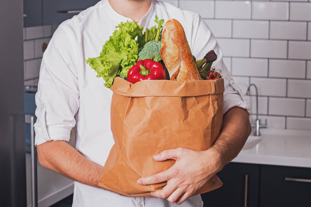Человек держит бумажный пакет с различными овощами и другими продуктами
 - Фото, изображение