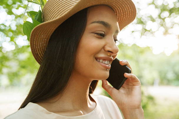 Photo of pretty woman wearing straw hat talking on smartphone in green park - Fotoğraf, Görsel