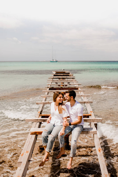 Encantados amantes sentados en el muelle destruido en la orilla del mar
 - Foto, imagen