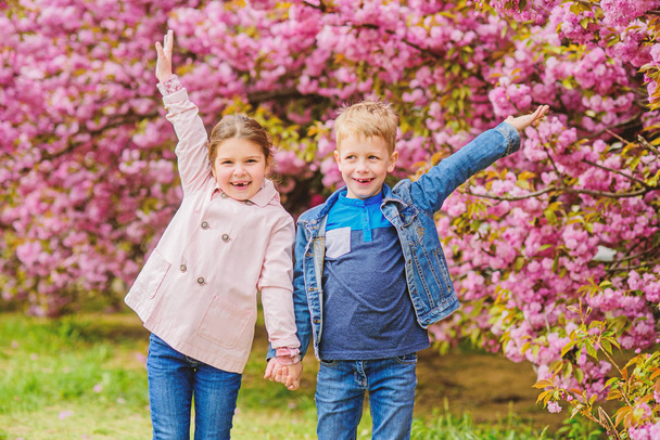 Couple kids walk sakura tree garden. Tender love feelings. Little girl and boy. Romantic date. Spring time to fall in love. Kids in love pink cherry blossom. Love is in the air. Romantic babies - Photo, Image