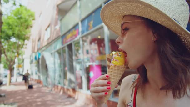 Young girl in a hat eating ice cream in the city - Video