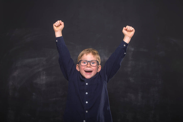 Happy school child boy in uniform and glasses against blackboard. Yeah! Strong kid raising hands up. Successful education. Stop bulling. - Photo, Image