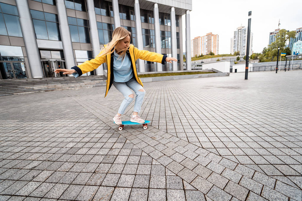 Blond female hipster woman riding on the longboard in the street at city. - 写真・画像