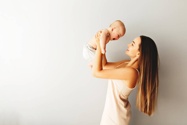 Beautiful mother holds her baby on a plain light background. - Foto, Bild