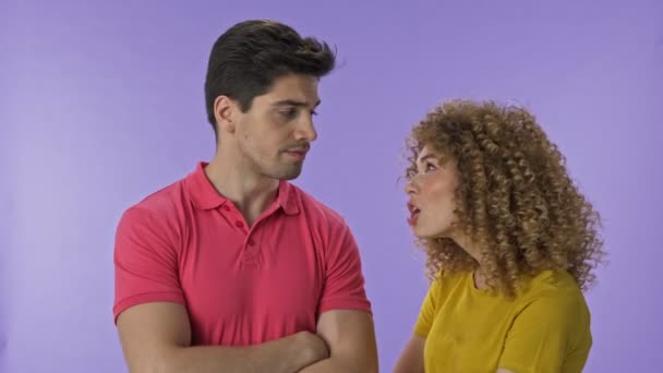 Beautiful young aggressive woman yelling at her boyfriend. Handsome young man becoming annoyed and making stop gesture with hand to his girlfriend and going away. Attractive young couple arguing with each other over purple background isolated - Imágenes, Vídeo