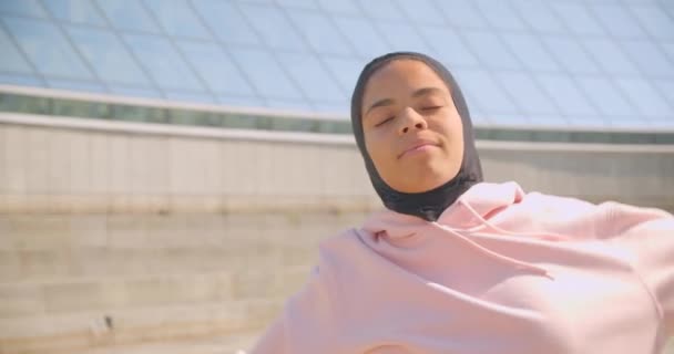 Closeup portrait of young cheerful african american muslim girl in hijab warming up on stadium urban city outdoors - Кадры, видео
