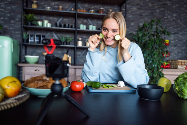 Young beautiful blonde takes on videos as she cooks in the kitchen - Fotoğraf, Görsel