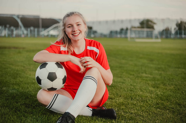 Портрет улыбающейся девушки футболистки с футбольным мячом, сидящей на траве, пространство для копирования
 - Фото, изображение