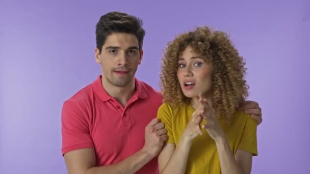 Attractive young lovely couple feeling worried and making winner gesture while becoming very happy over purple background isolated  - Imágenes, Vídeo
