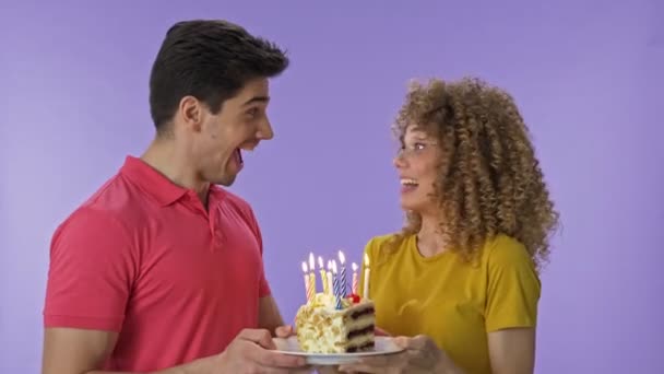 Happy young lovely couple celebrating a birthday together and blowing out the candles on cake over purple background isolated - Filmmaterial, Video