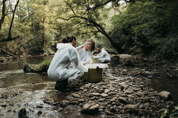 Scientists biologists and researchers in protective suits taking water samples from polluted river. - Fotografie, Obrázek