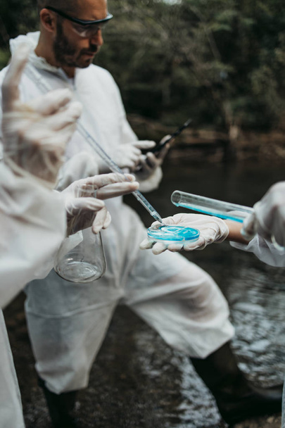 Scientists biologists and researchers in protective suits taking water samples from polluted river. - Φωτογραφία, εικόνα