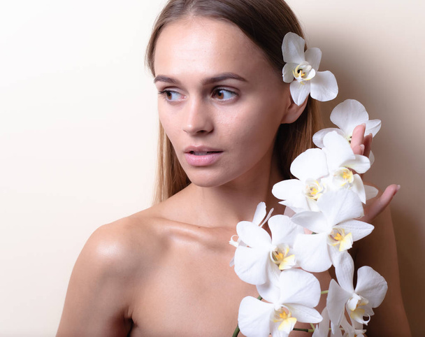 Κοντινό πορτρέτο ενός όμορφου μοντέλου με λευκά λουλούδια ορχιδέα. - Φωτογραφία, εικόνα