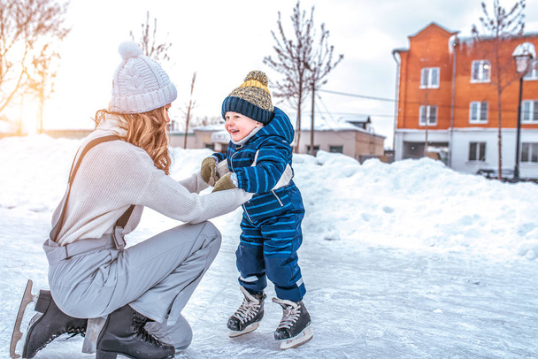 Mom with baby boy 3-5 years old, learn to train, ride in winter city on rink, ice skating. Happy smiling children play having fun weekend weekend first steps child ice skating. Free space for text. - Foto, Imagen