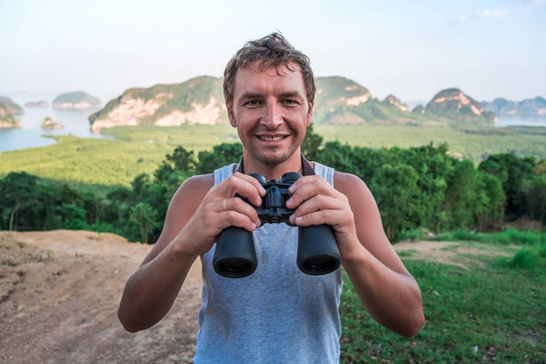 Cheerful young man with binoculars on the background of rocks and the sea - Foto, Bild