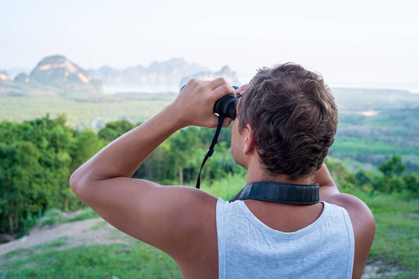 Young man at the top is looking at the rocks through binoculars - Фото, изображение