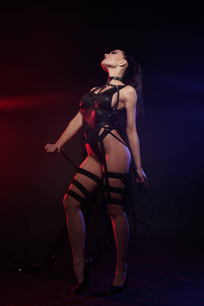 beautiful mix race slender muscular dancer girl posing in a black swimsuit with leather harness with videotape tapes - 写真・画像