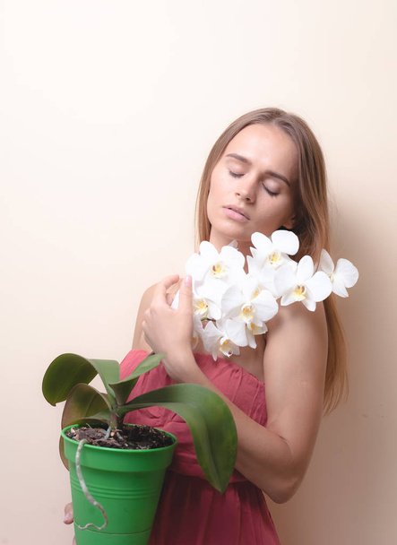 Portrait of a beautiful girl with an orchid on a light background. - Photo, Image