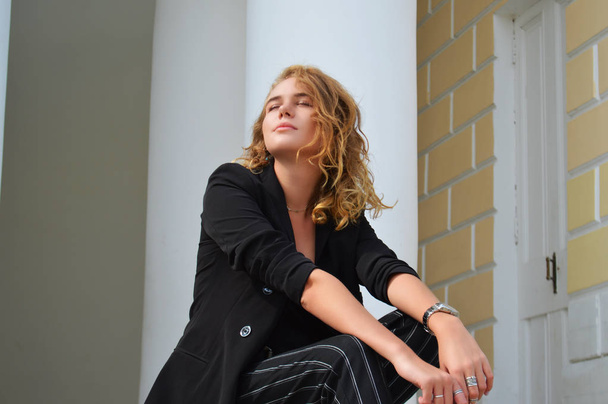 Een sexy jonge vrouw in een Business Black Suit zit - Foto, afbeelding