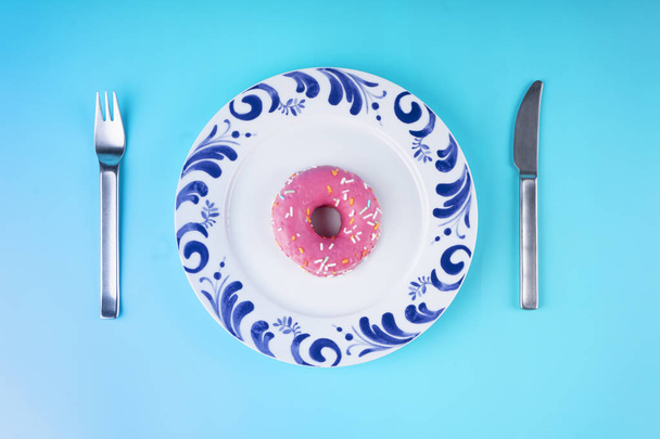Donuts glaze on plate and cutlery on blue background - Фото, изображение