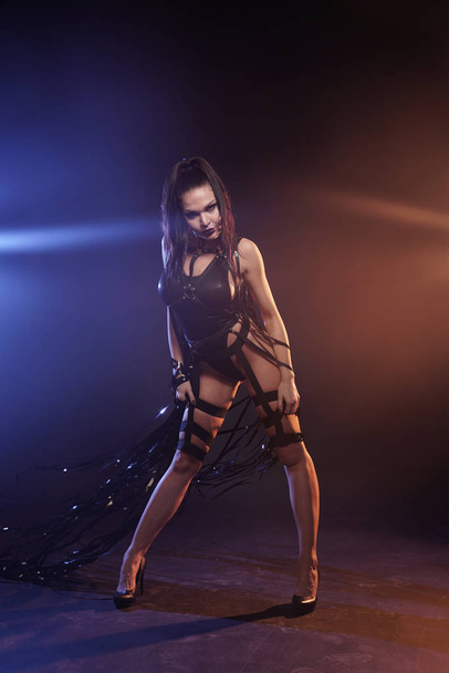 красива мікс гонка струнка м'язиста дівчина-танцюрист позує в чорному купальнику з шкіряним джмелем зі стрічками відеокасети
 - Фото, зображення