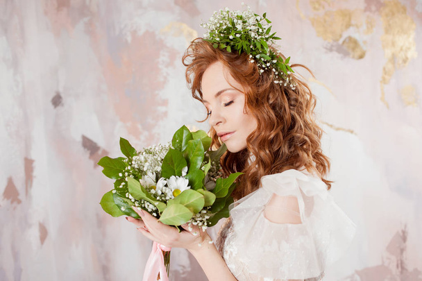 Portrait of a young beautiful woman in wedding dress with wreath and bouquet of fresh flowers. - Фото, зображення
