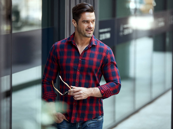 Young handsome man in plaid shirt and jeans posing on urban background - Foto, imagen