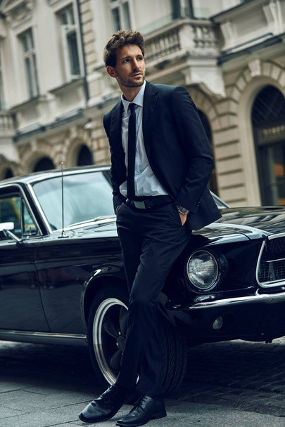 Young handsome man with black classic car wearing black suit  - Fotó, kép