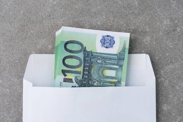 Biała koperta z banknotami 100 euro. Stos stu banknotów euro w otwartej kopercie pocztowej betonu. Banknoty euro złożone w kopercie jako prezent. Wysyłanie lub oszczędzanie pieniędzy, koncepcja korupcji - Zdjęcie, obraz