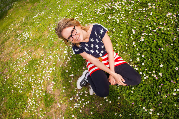junge Frau mit Brille, die entspannt auf dem Gras sitzt und in die Kamera blickt. Konzept friedlicher Lebensstil - Foto, Bild