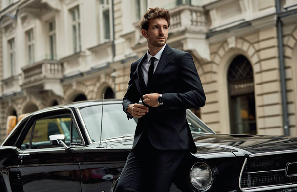 Young handsome man with black classic car wearing black suit  - Фото, изображение