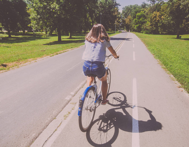 Bonita jovem mulher andar de bicicleta no parque vista traseira
 - Foto, Imagem