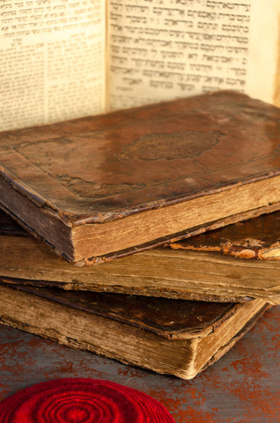 Joodse Bijbel. Een stapel oude leer-gebonden Joodse boeken met goud stampen, een open boek en rode gebreide Joodse baal. Selectieve focus - Foto, afbeelding