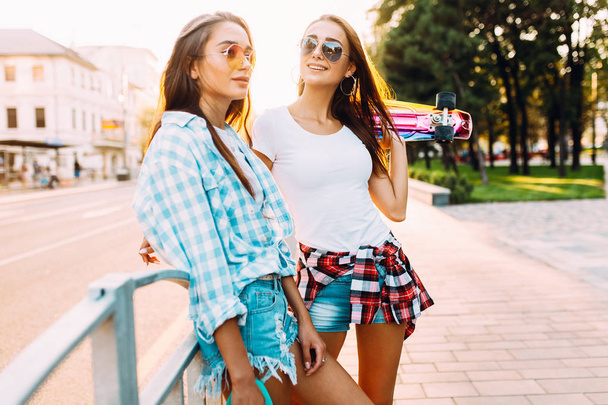 Two cheerful young girls in shorts , friends pose standing with  - Φωτογραφία, εικόνα