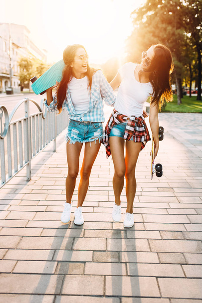 Two cheerful young girls walking with skateboards in the Park - Фото, изображение