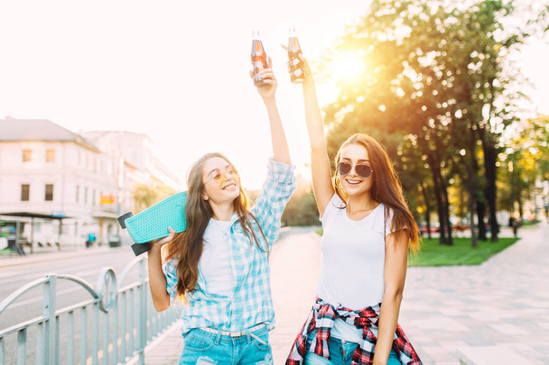 Two girlfriends in sunglasses, drink a drink and walk down a cit - Fotoğraf, Görsel