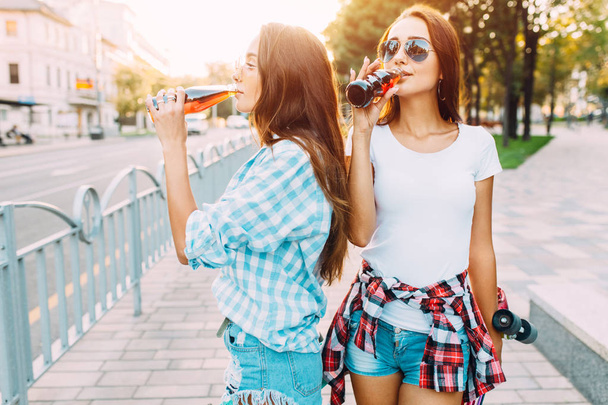 Two girlfriends in sunglasses, drink a drink and walk down a cit - Fotoğraf, Görsel
