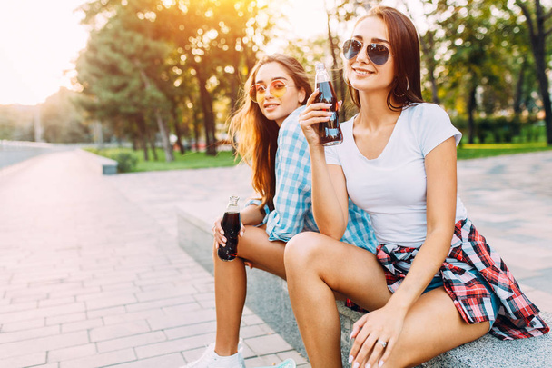 Two stylish girlfriends , drink a drink sitting in the Park - Фото, изображение