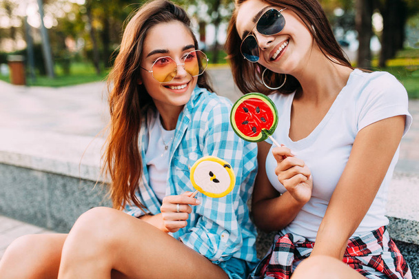 Two young stylish women sitting on a skateboard with lollipops h - Photo, image