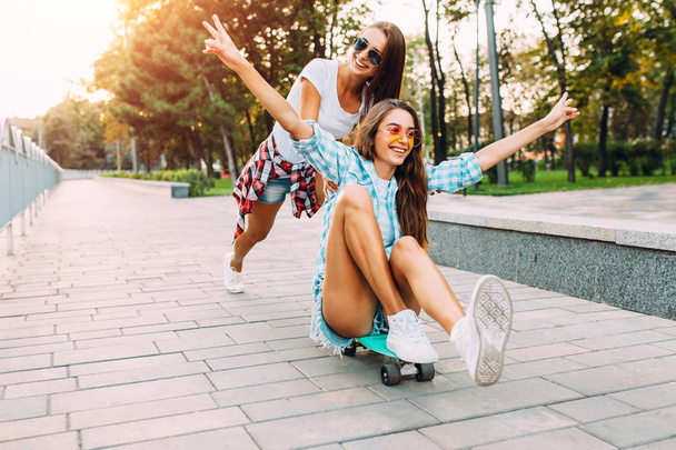 Two stylish excited girls have fun and skateboard in the Park in - 写真・画像